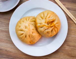 There is portion of Asian baozi xiaolongbao pan chino dumplings on table - large shaped balls stuffed with minced meat. Dish is served with hot soy sauce, light alcohol