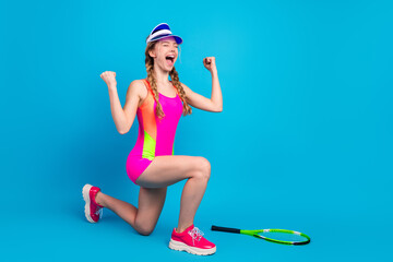 Young woman in vibrant sportswear celebrating victory with raised arms, kneeling on one knee