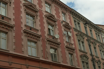 The facade of a wellpreserved historical building showcases numerous charming windows, intricate architectural details, and modern satellite dishes set against a bustling urban environment