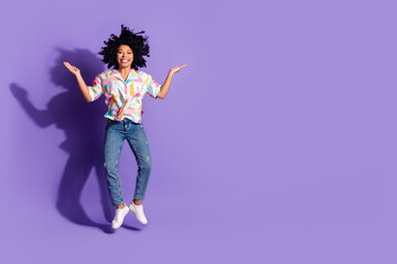Happy woman jumps joyfully in stylish casual outfit against bright violet background, expressing...