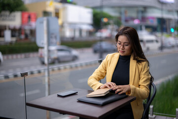 Fototapeta premium A woman in a yellow jacket is sitting at a table with a book and a cell phone