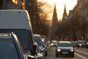 In this vibrant scene, vehicles are stuck in slow traffic, bathed in a warm sunset, with grand...