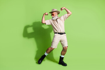 Energetic senior explorer in safari attire flexing muscles against a vibrant green background