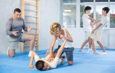 Willing junior attendee of self-defense classes practicing arm twist on a lying boy in sports hall