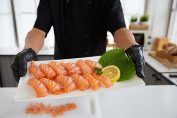 close up chef holding and showing salmon sushi on white plate