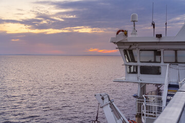 A stunning sunset casts vibrant colors across the sea while the ferry cruise ship sails through the tranquil Kattegat Strait, with the bridge in view.
