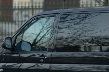 A closeup shot of a sleek, stylish black van featuring tinted windows that beautifully reflect the...