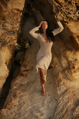 Elegant Brunette in Crochet Dress Posing by Textured Rocks at Sunset