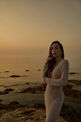 Elegant Brunette in Crochet Dress Posing by Textured Rocks at Sunset