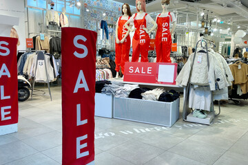 A retail store interior showcasing a sale. Mannequins in red outfits display sale signs. Clothing...
