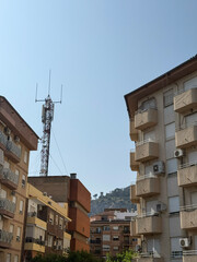 Urban landscape with residential buildings and a telecommunications tower under a clear blue sky. The scene captures modern architecture and city life.