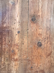Close-up of a rustic wooden surface with visible grain patterns and knots. The wood has a warm brown tone, showcasing natural textures and imperfections.