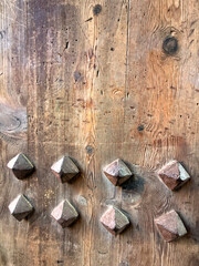 A close-up view of a wooden door with decorative metal studs. The wood has a rustic texture, showcasing natural grain patterns and knots.
