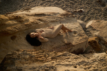 Elegant Brunette in Crochet Dress Posing by Textured Rocks at Sunset