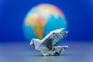 An origami bird folded from a US dollar bill and a globe. International financial transfers,...