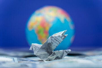 An origami bird folded from a US dollar bill and a globe. International financial transfers,...