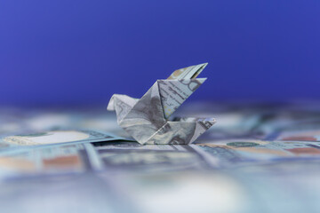 An origami bird folded from a US dollar bill on a blurred bed of more dollar bills. Financial...