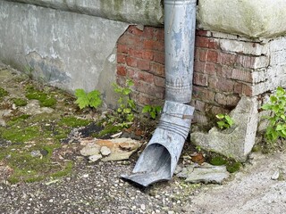 A Rusty Drainpipe Featuring a Weathered Texture Situated Against an Old Brick Wall. An old drainpipe contrasts with aged bricks, highlighting rustic textures among the nearby lush greenery