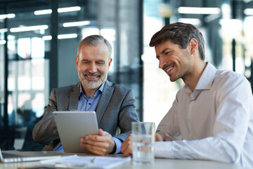 Mature businessman using a digital tablet to discuss information with a younger colleague in a modern business office