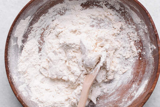 Overhead view of paratha dough being mixed in a wooden bowl, top view of flaky flatbread dough in a wood bowl, process of making paratha