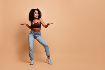 Stylish young woman with curly hair in casual outfit posing confidently on a beige background