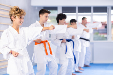 Diligent preteen attendee of karate classes practicing kata standing in row with others in sports...