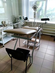  chair in ginecological office in the hospital. Tiles on the walls and floor, blinds on the window, chair and lamp for examination, tables for instruments