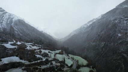 Serene mountain valley shrouded in mist and early winter snowfall, with a winding country road leading through the frosty scenery, conveying peaceful nature and adventure.