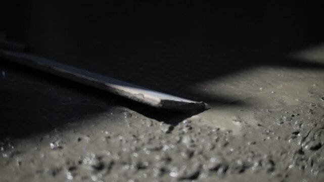 Freshly poured concrete being leveled at construction site