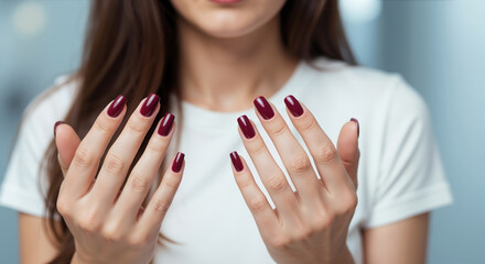 Woman showing burgundy manicured nails with both hands extended forward in white shirt. Professional nail care and manicure services for beauty salon treatments and cosmetic enhancement