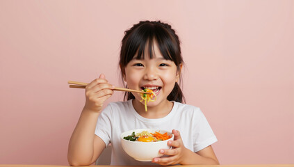 Asian girl eating noodles with chopsticks from white bowl on pink background while smiling. Traditional asian cuisine for family meals and cultural dining