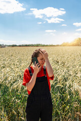 farming problems. Female farmer reacting to phone call in cereal field with hand on forehead