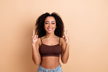 Obraz premium Portrait of a young woman with curly brown hair wearing casual clothing, smiling in a stylish pose against a beige background
