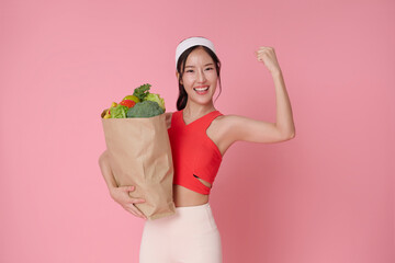 Young beautiful asian sporty woman with sportswear holding grocery shopping bag isolated on pink background. Portrait wellness food healthy lifestyle.