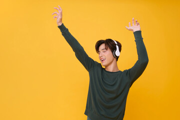 Happy young asian man listening to music with headphone dancing isolated on yellow background. People lifestyle relax concept.