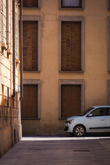 Reggio Emilia, Italy, 01.04.2025. Small light blue car parked near aged building facade with brown closed shutters