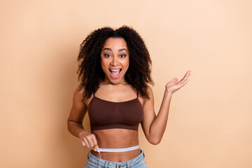 Young woman measuring her waist in a cheerful moment against a beige background wearing casual and...