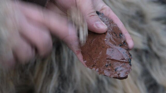 A craftsman uses an antler tool for pressure flaking to sharpen a prehistoric flint tool. A close-up on ancient technology and survival skills.