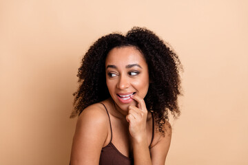 Attractive young woman with curly hair showcasing her vibrant style against a beige background,...