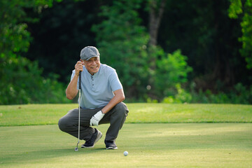Senior golfer crouching on green grass, focusing on golf ball alignment before putting. Concept of concentration, strategy, and active lifestyle for older adults in outdoor sports.