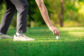 Hand golfer putting golf ball on tee with club in golf course on evening and sunset time a for healthy sport. Lifestyle Concept.