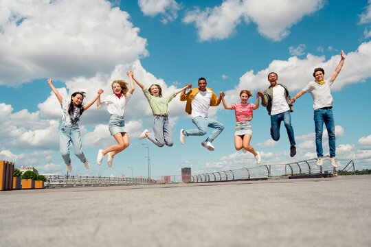 Group of cheerful friends jumping together outdoors during a sunny day, showcasing friendship and youthful energy
