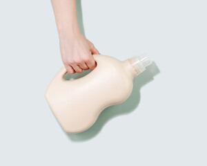 Hand Holding Neutral-Toned Laundry Detergent Bottle On Blue Background With Soft Shadow. Concept Of...