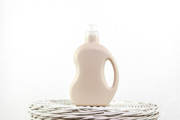 Beige Laundry Detergent Bottle Standing On Wicker Surface Against White Background In Soft Light. Concept Of Sustainable Packaging, Home Care Trends, And Ideal Mockup For Label Design Projects