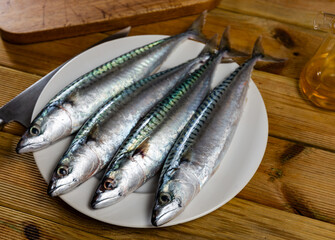 Fish carcasses for cooking are prepared on table. Four whole mackerels lie on plate near cutting...