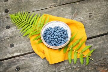 Bowl Of Fresh Blueberries On Yellow Cloth With Fern Leaves Over Rustic Wooden Table. Concept Of...