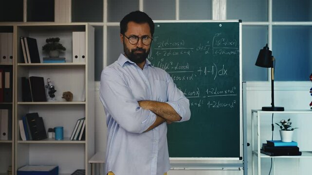 Portrait of serious middle-aged male math teacher standing near chalkboard