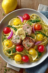  Plato de pasta espagueti con medallones de atún, tomates cherry amarillos y rojos, espárragos, rodajas de limón y cebolla morada.

