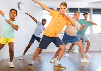 Dynamic little boy training Hip hop dance poses in dancehall with other attendees of dancing courses