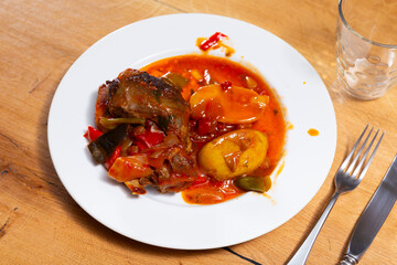 Baked unpeeled potato and pieces of pork chop with samhain sauce gravy are served on table. Vegetable dish stew from chef of restaurant is prepared according to recipe of Catalan cuisine.